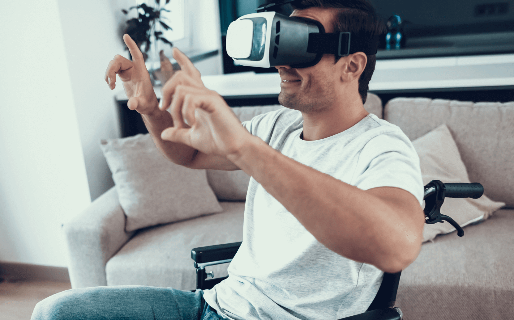 Smiling man in a wheelchair wearing a VR headset and gesturing with both hands in a living room