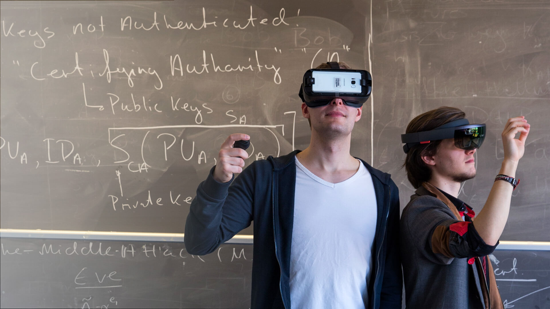 Two students at a chalkboard, one in a mobile VR headset and the other wearing a HoloLens