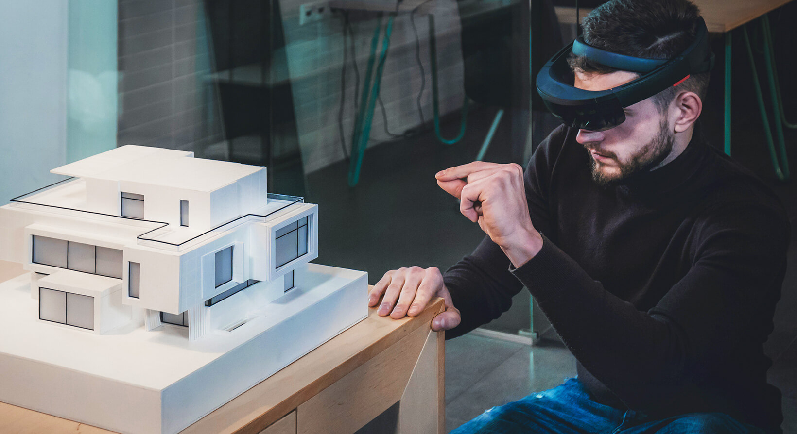 Architect in a HoloLens headset gesturing beside a white scale model of a modern house