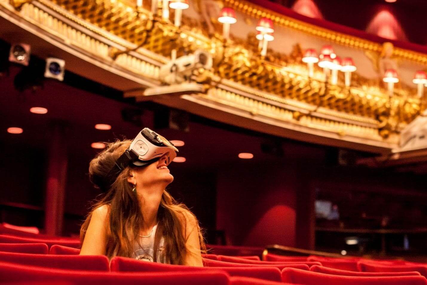 Woman in a VR headset sitting in the red velvet stalls of an ornate theatre