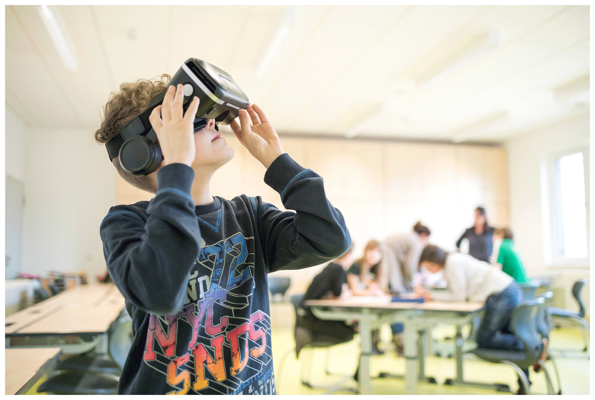 Boy in a VR headset looking up in a classroom while other pupils work at desks behind him