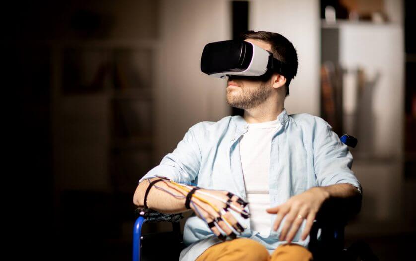 Man in a wheelchair wearing a VR headset and a glove wired with sensors
