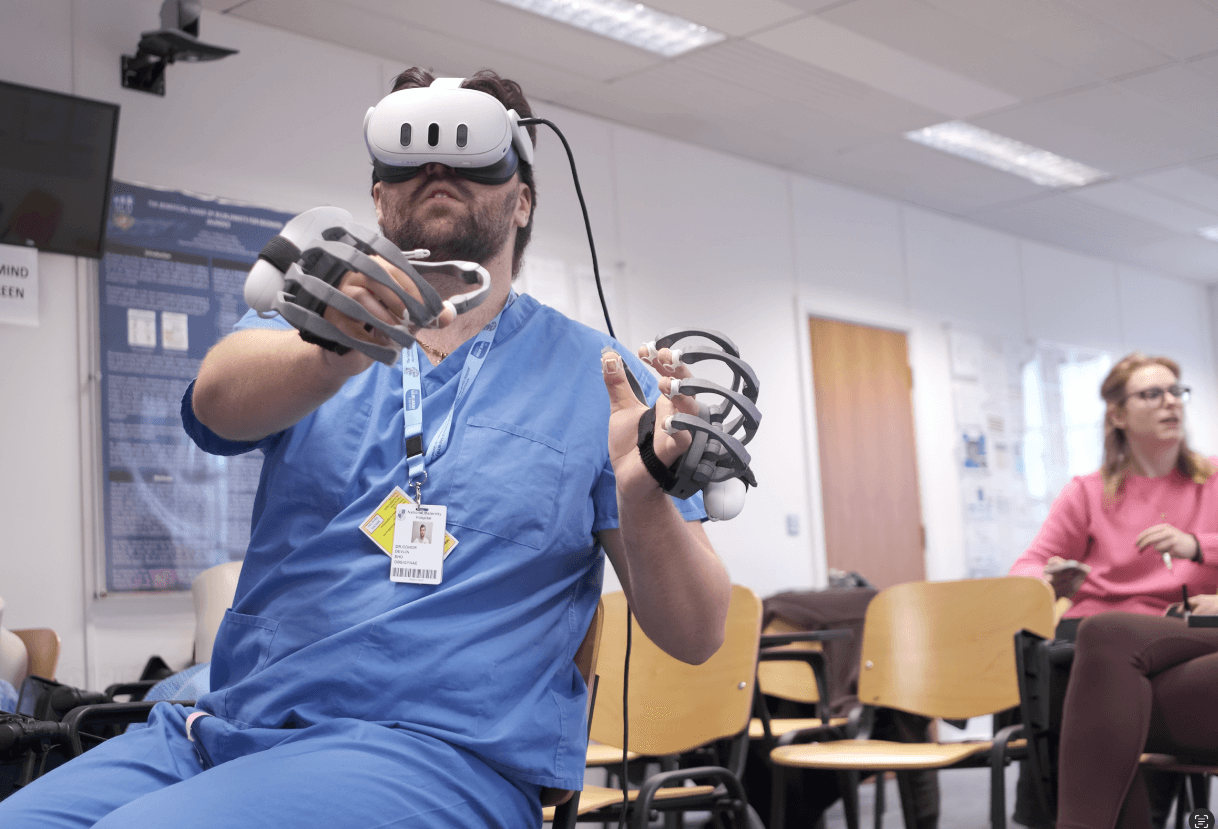 Clinician in scrubs wearing a Meta Quest 3 headset and haptic gloves while a colleague watches