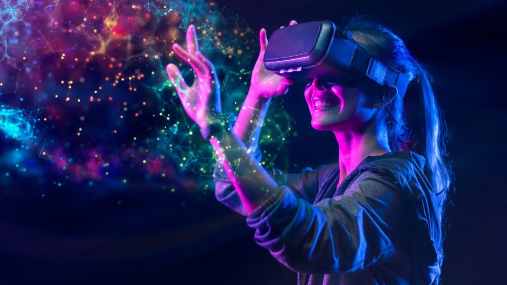 Smiling woman in a VR headset reaching into a cloud of glowing coloured particles